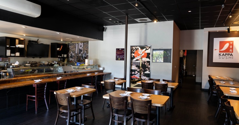 Interior of a sushi restaurant with tables and chairs, a wooden counter, and a colorful screen