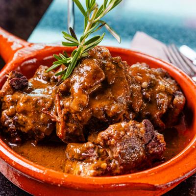 Spanish oxtail stew featuring braised beef pieces in brown gravy with rosemary garnish.
