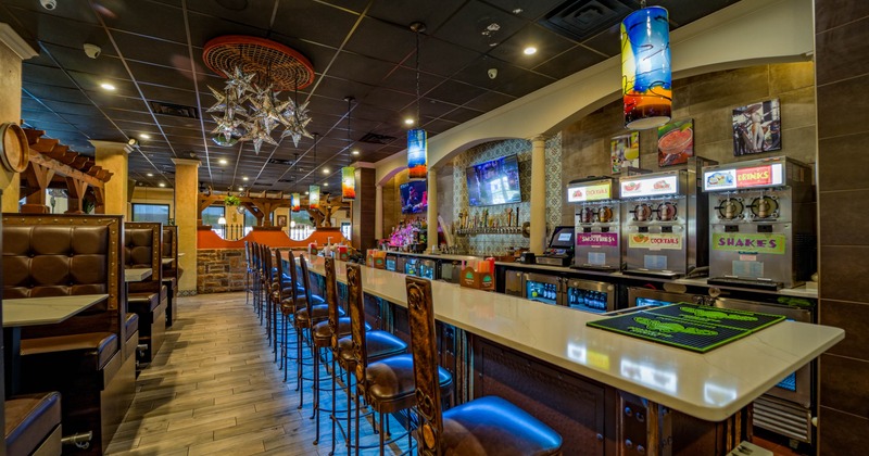 Interior of a restaurant featuring a bar with leather stools, beverage dispensers