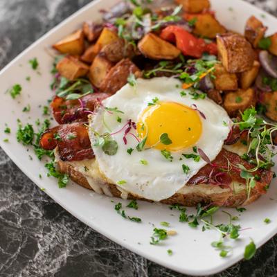 Bread topped with melted cheese, bacon, sunny egg, and served with potatoes