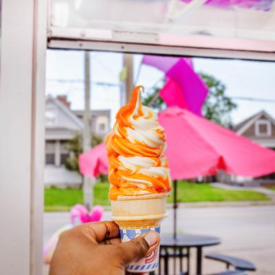 A hand holding a sherbet cone against a vibrant pink umbrella background.