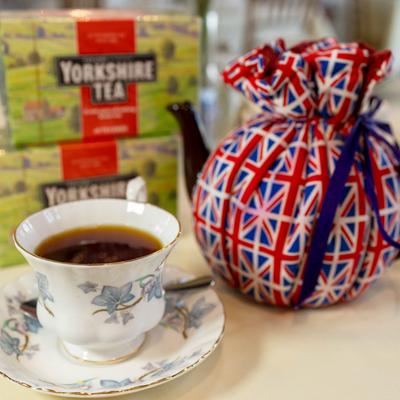 A cup of tea beside a teapot wrapped in Union Jack fabric and Yorkshire tea boxes.