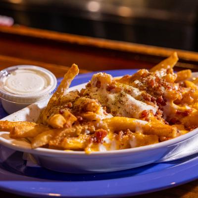 Loaded fries topped with melted cheese and bacon, served with a side of dipping sauce.