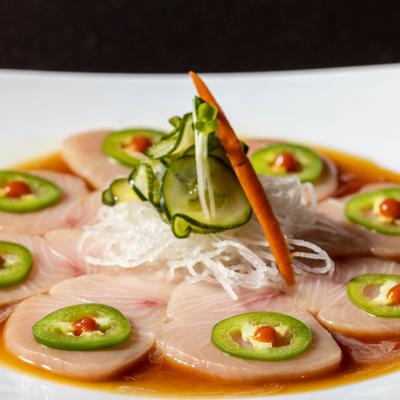 Yellowtail sashimi with jalapeno slices and sauce.