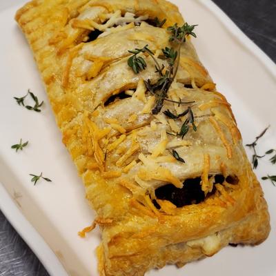 A golden-brown pastry with lattice cuts, topped with grated cheese and sprigs of fresh thyme.