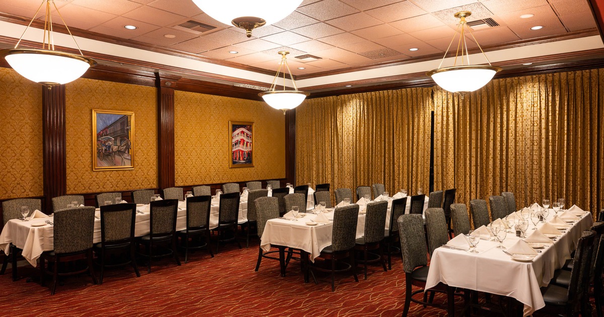 Inside. elegant dining room with long tables, gold walls, red carpet, and large light fixtures