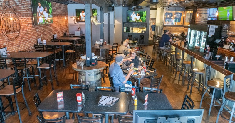 A dimly lit bar and restaurant with exposed brick walls and televisions displaying sports