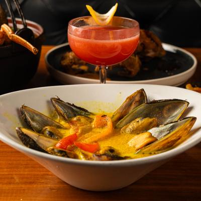 Bowl of mussels served on the table with a cocktail.