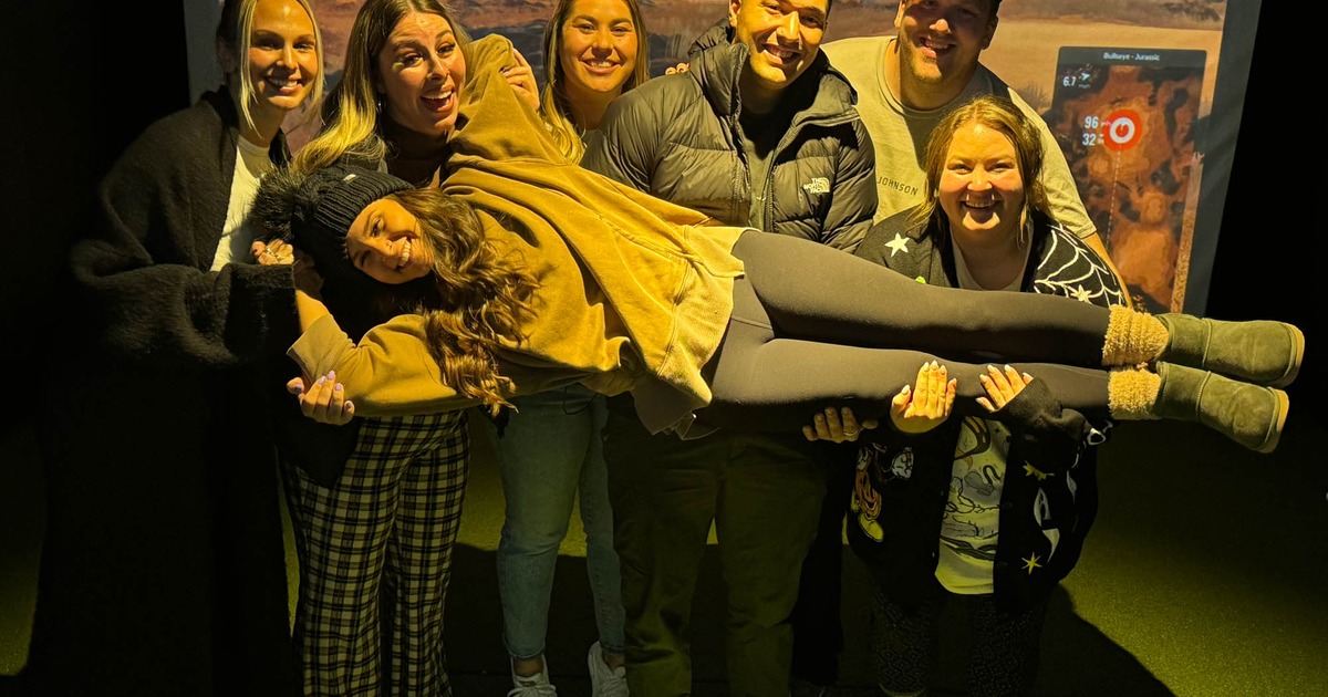 A group of people smiling and posing for a shot in front of a simulator screen