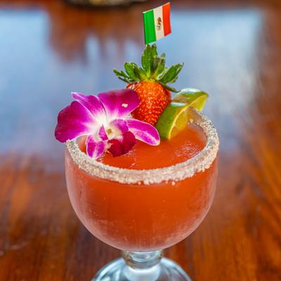 Strawberry Margarita garnished with a lime, a strawberry, pink orchid and small Mexico flag.
