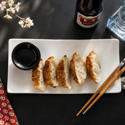 Pan-fried gyoza dumplings are served on a plate with dipping sauce.