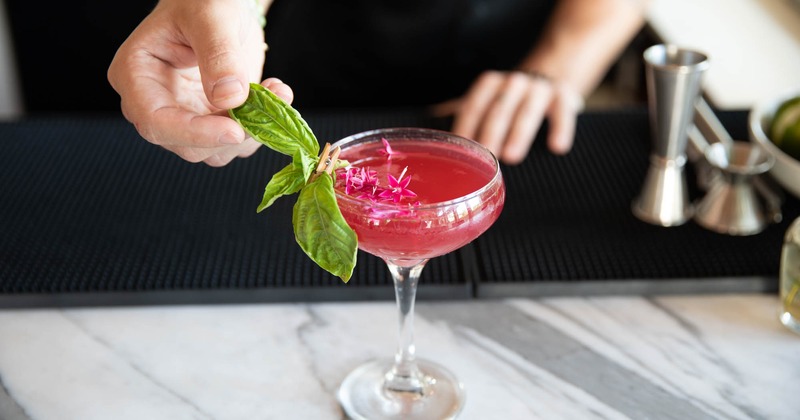 Bartender places leaf garnish on a cocktail glass, hands closeup