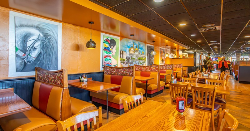 Restaurant interior with wooden tables, booth seating, and vibrant artwork on orange walls