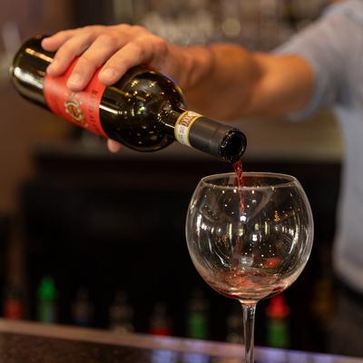 Bartender pouring red wine into a wine glass.