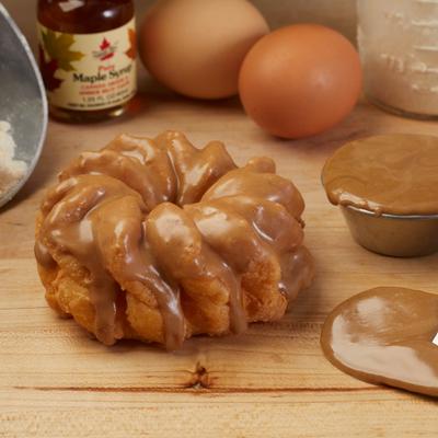 Maple cruller pastry on a wooden board beside fresh eggs and caramel sauce.