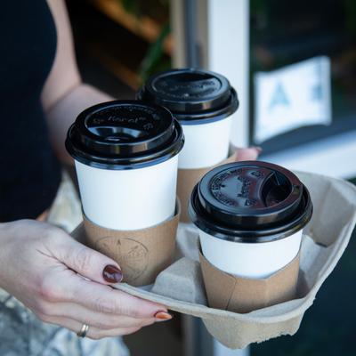 Person holding a cardboard drink carrier with three disposable coffee cups.