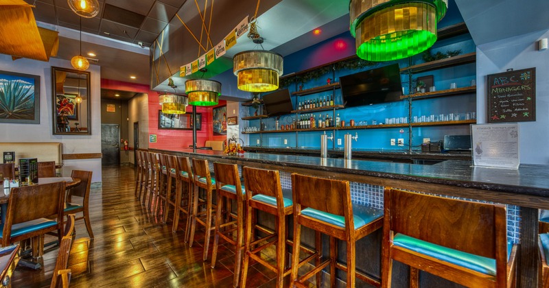 Interior of a colorful bar and restaurant with a long wooden bar counter, tall wooden chairs