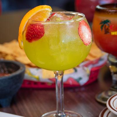 Sour Apple Margarita with an orange wedge and strawberry slices.