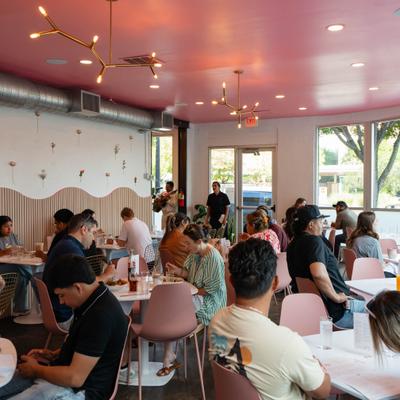 Guests dining in a busy cafe with a pink ceiling and pink chairs.