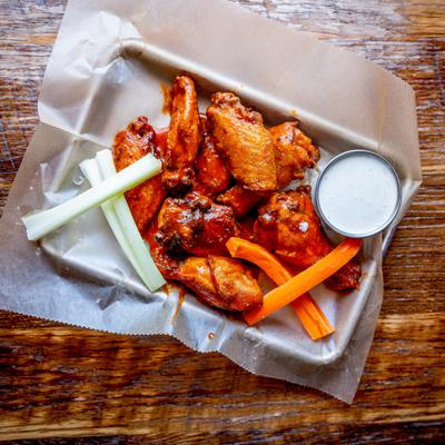 A tray of saucy buffalo wings with celery, carrots, and ranch.