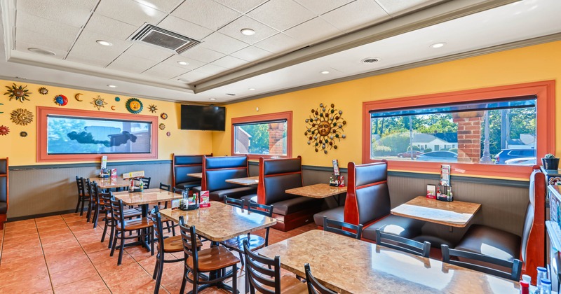 Bright restaurant dining room with yellow walls, decorative sun artwork, booths, tables