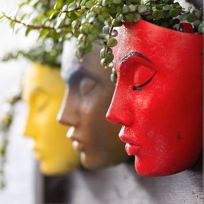 Three red and yellow face planters filled with trailing plants.