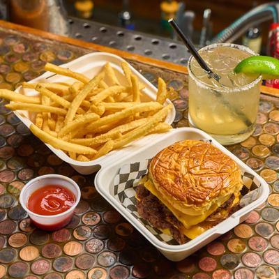 Cheeseburger served with fries and a dipping sauce, alongside a Margarita cocktail.
