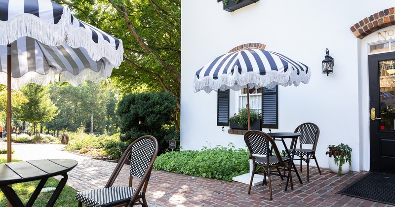 An outdoor patio with round tables for two guests and a black-and-white striped umbrella