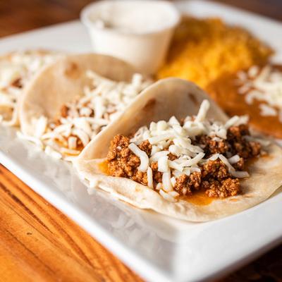 Beef cheese tacos served with sour cream, rice and refried beans, close up.