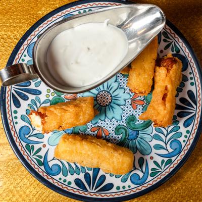 Mozzarella sticks served with a metal boat filled with a white dipping sauce.