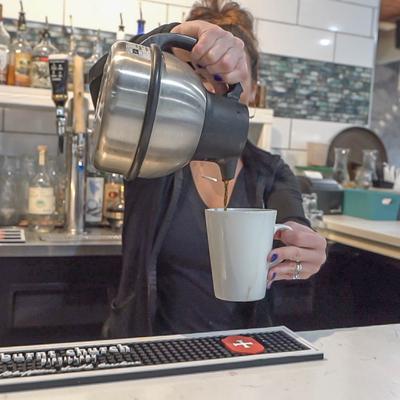 Barista pouring coffee from a metal thermos into a white mug