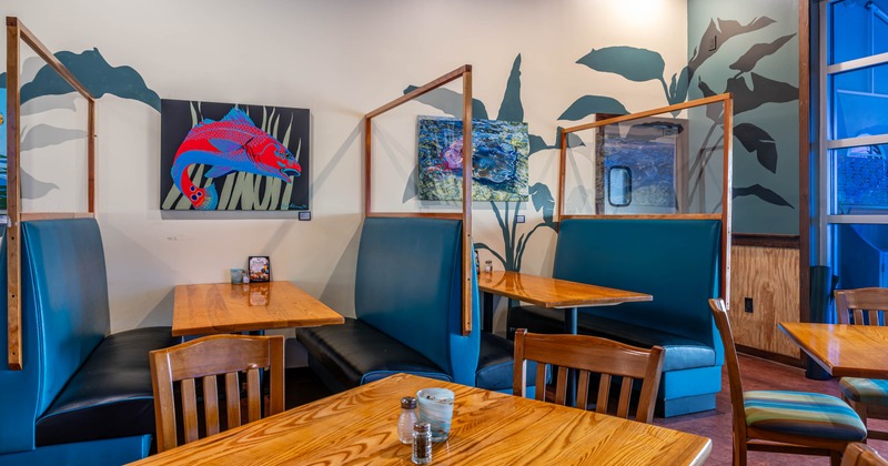 Interior, wooden tables and chairs, teal booth seating, and vibrant marine themed artwork