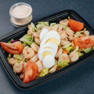 Shrimp salad topped with hard-boiled egg and tomatoes, served with two cups of dressing.
