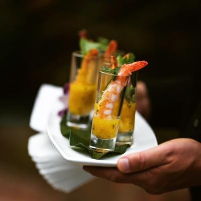 Hands holding a plate of mango shrimp shooters.