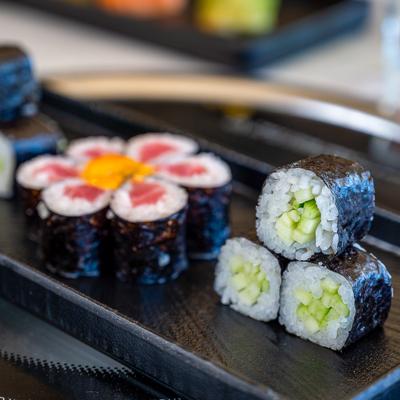 Cucumber rolls and tuna rolls arranged in a flower shape served on a black tray.