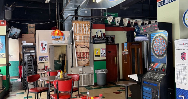 Retro-themed bar with red chairs, a round table, a checkerboard tile floor, and various signs.
