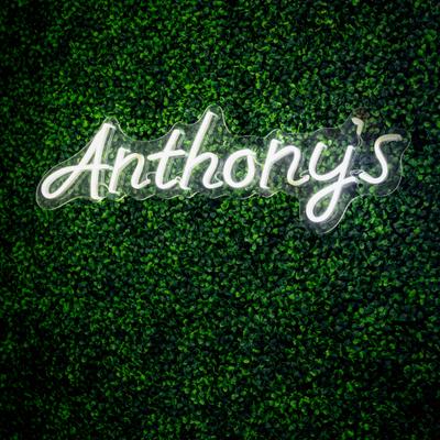 Neon restaurant sign on a green hedge wall.