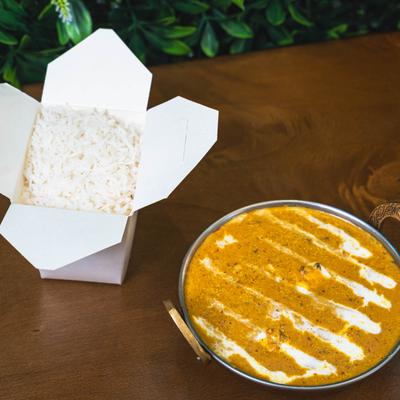 Indian curry with white rice in a takeout box on a wooden table.