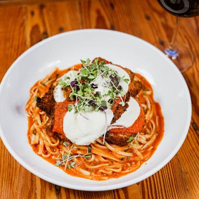 A plate of Chicken Parmesan with linguine, served on a wooden table