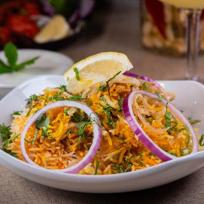 Chicken Biryani garnished with onions, herbs and a lemon wedge.
