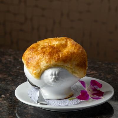 Mussel bisque served in a white lion-head bowl with flower.