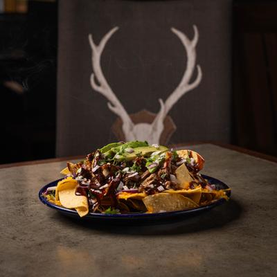 BBQ nachos topped with diced onions and avocado slices, served on the table.