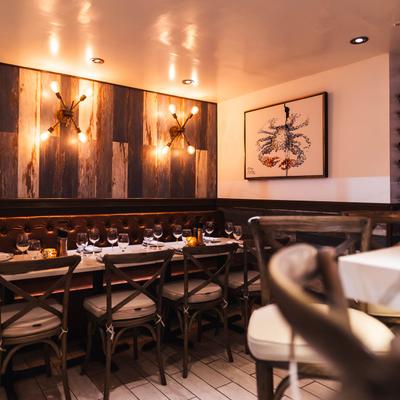 Interior, cozy banquet seating with tableware and glasses on tables and chairs.