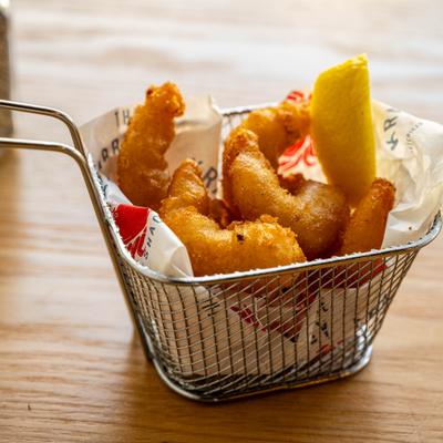 Fried shrimp served in a small wire basket with a lemon wedge.