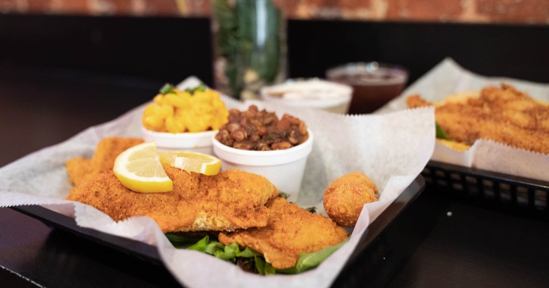 A basket with fried fish and sides of baked beans and mac and cheese