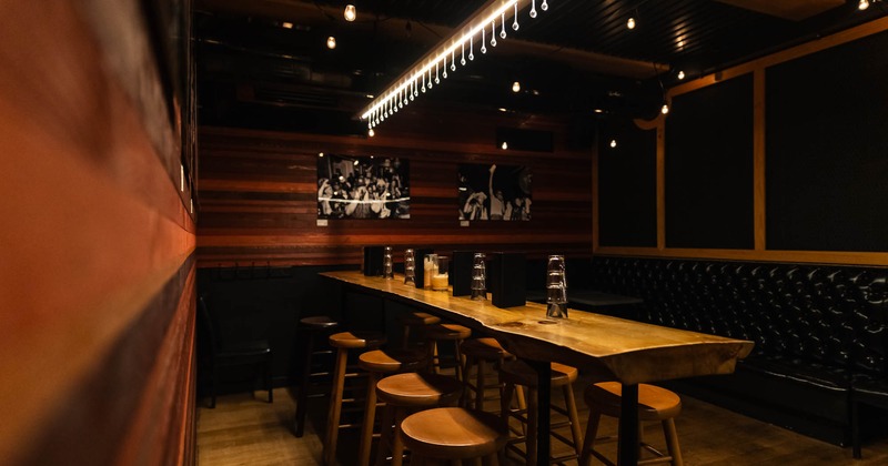 Interior of a dimly lit dining area with a long wooden table, bar stools