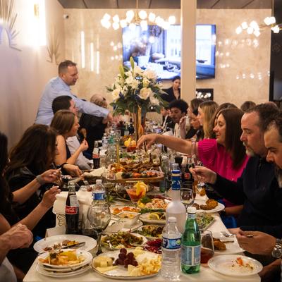 Large group of people dining at a long table with shared dishes and drinks.