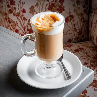Foamy latte served in a clear glass mug on a white saucer.