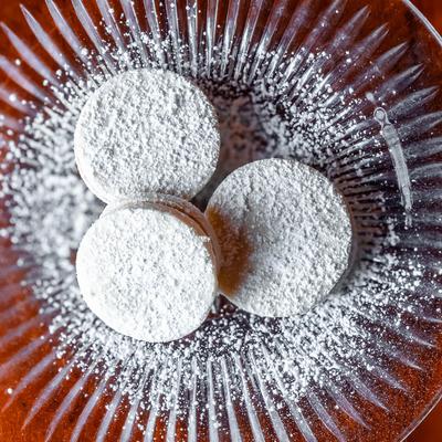 Overhead view of Peruvian shortbread sandwich cookies with powdered sugar on a glass plate.