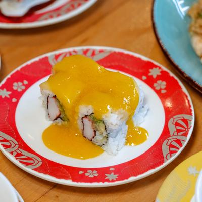 Happy mango roll sushi with bright yellow sauce on a red and white plate.
